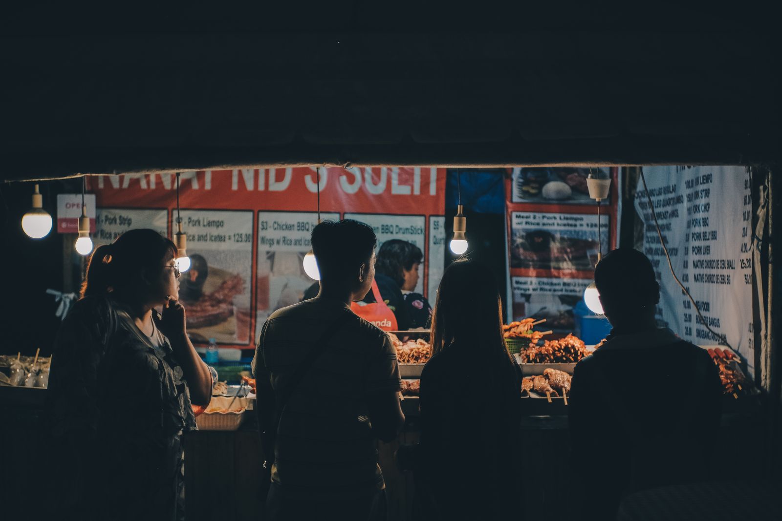 People silhouetted against the warm lights of night food stalls in Cebu City